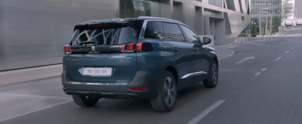 Un SUV Peugeot verde acqua che percorre una strada cittadina con edifici moderni sullo sfondo