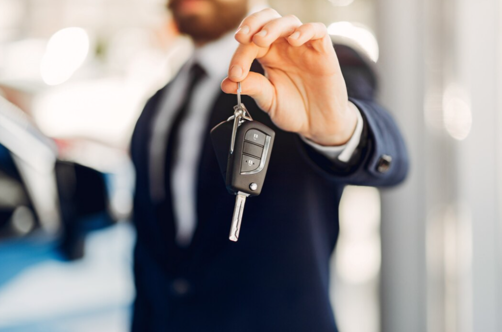 A man in a suit holds up car keys in a showroom setting